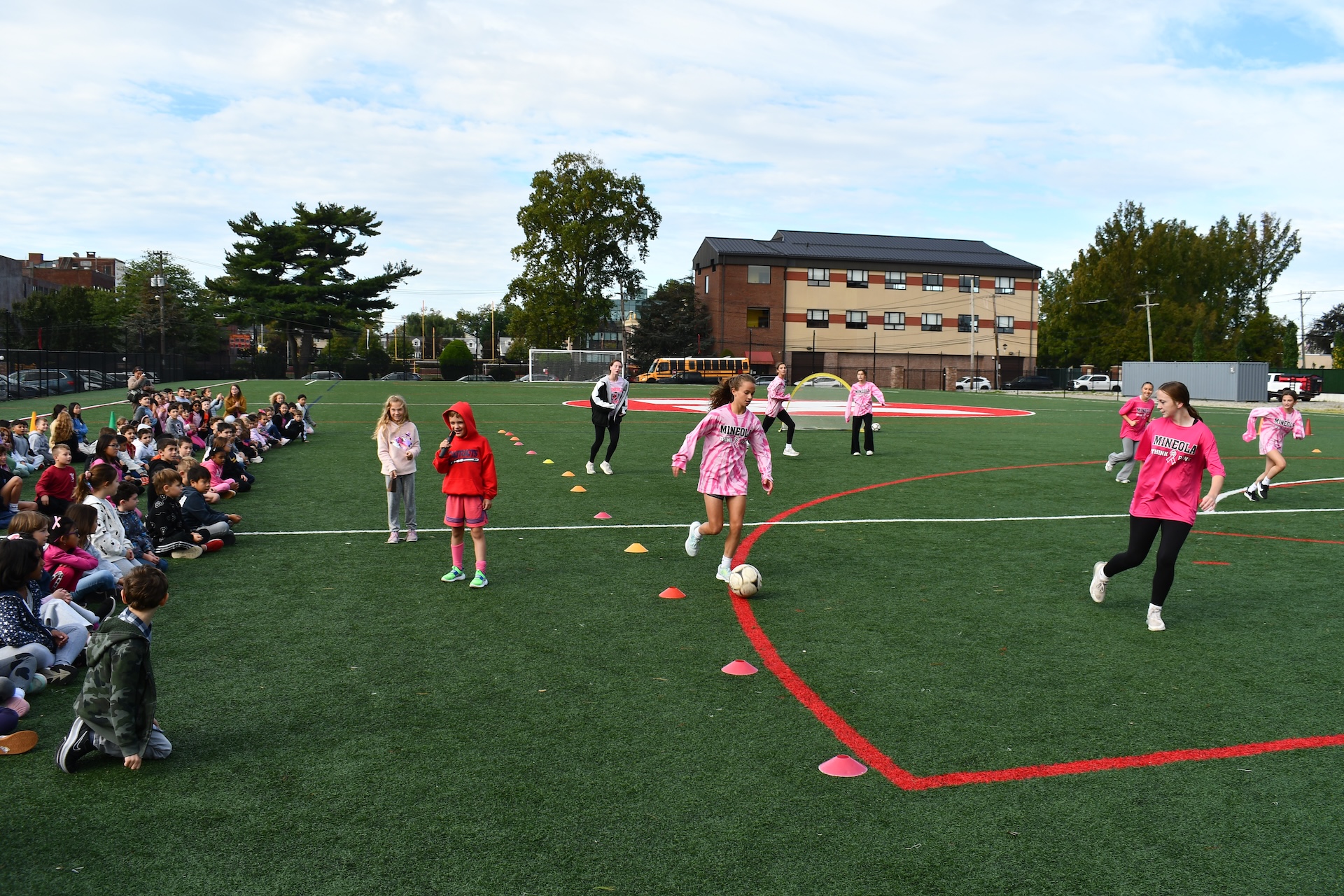 Elementary school student watching high school students play soccer on a turf field